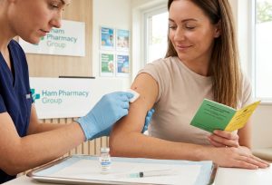 Woman receiving a vaccination from a healthcare professional at a pharmacy clinic while holding an immunisation record booklet.