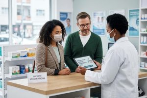Pharmacist showing a couple a tablet about private COVID boosters available in 2026 at a pharmacy private vaccinations counter